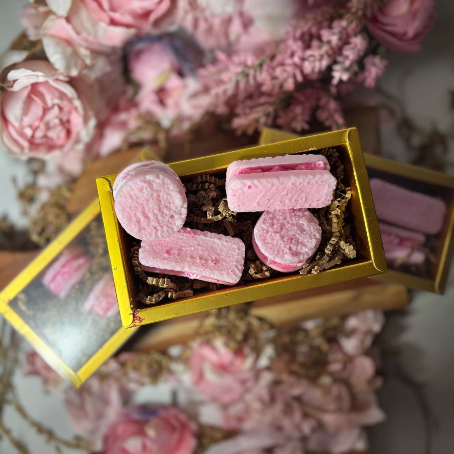 Box of pink French macaroons surrounded by flowers, showcasing wax melts with a delightful fruity scent.