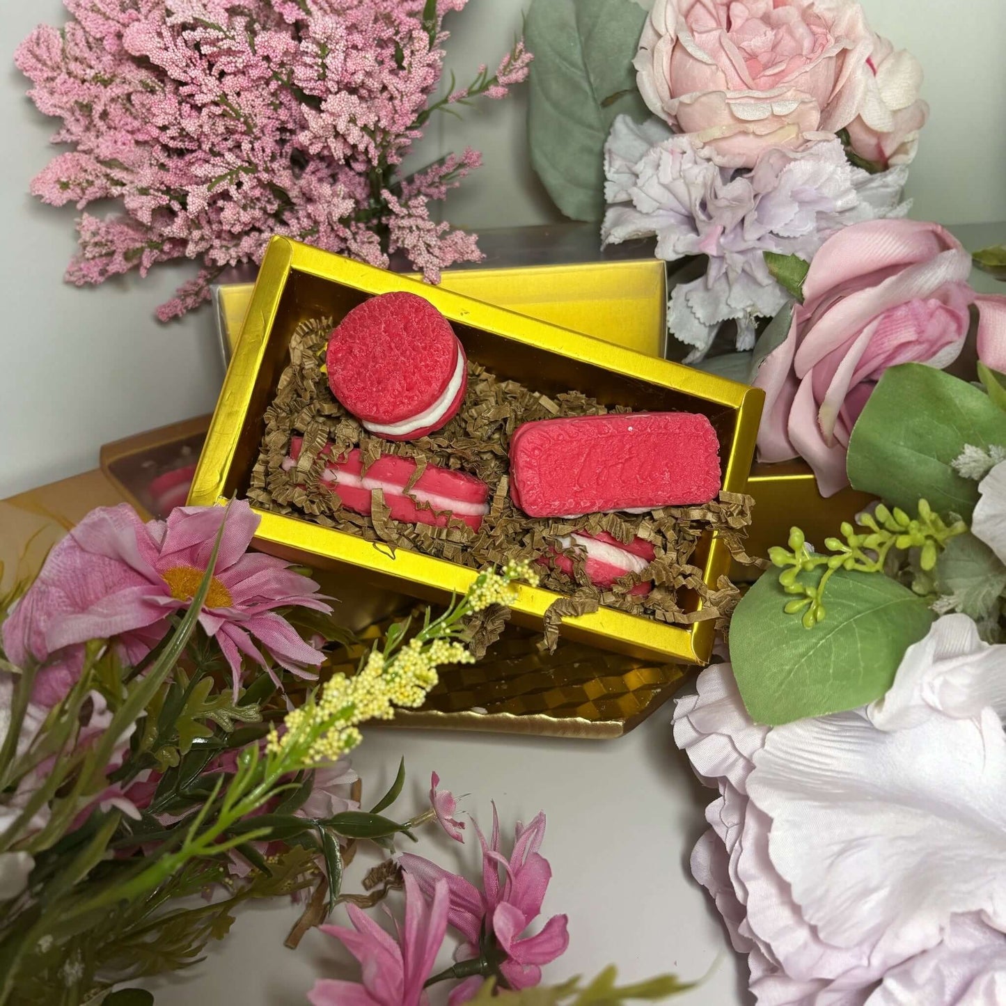 Colorful wax melts in a gold gift box surrounded by flowers, showcasing vibrant pink and red designs.